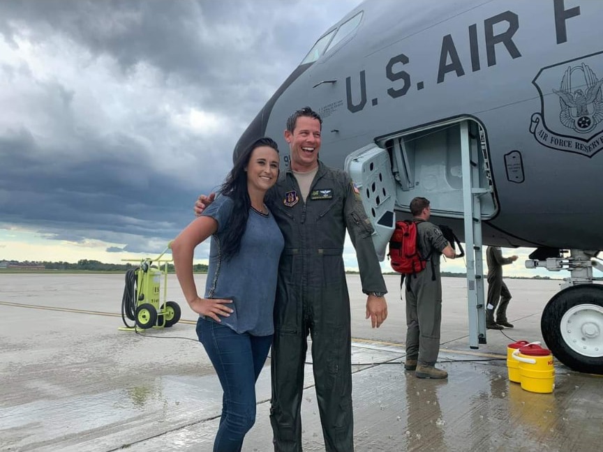 Nikki laughing with Quentin beside an Air Force Reserve KC-135 under storm clouds.