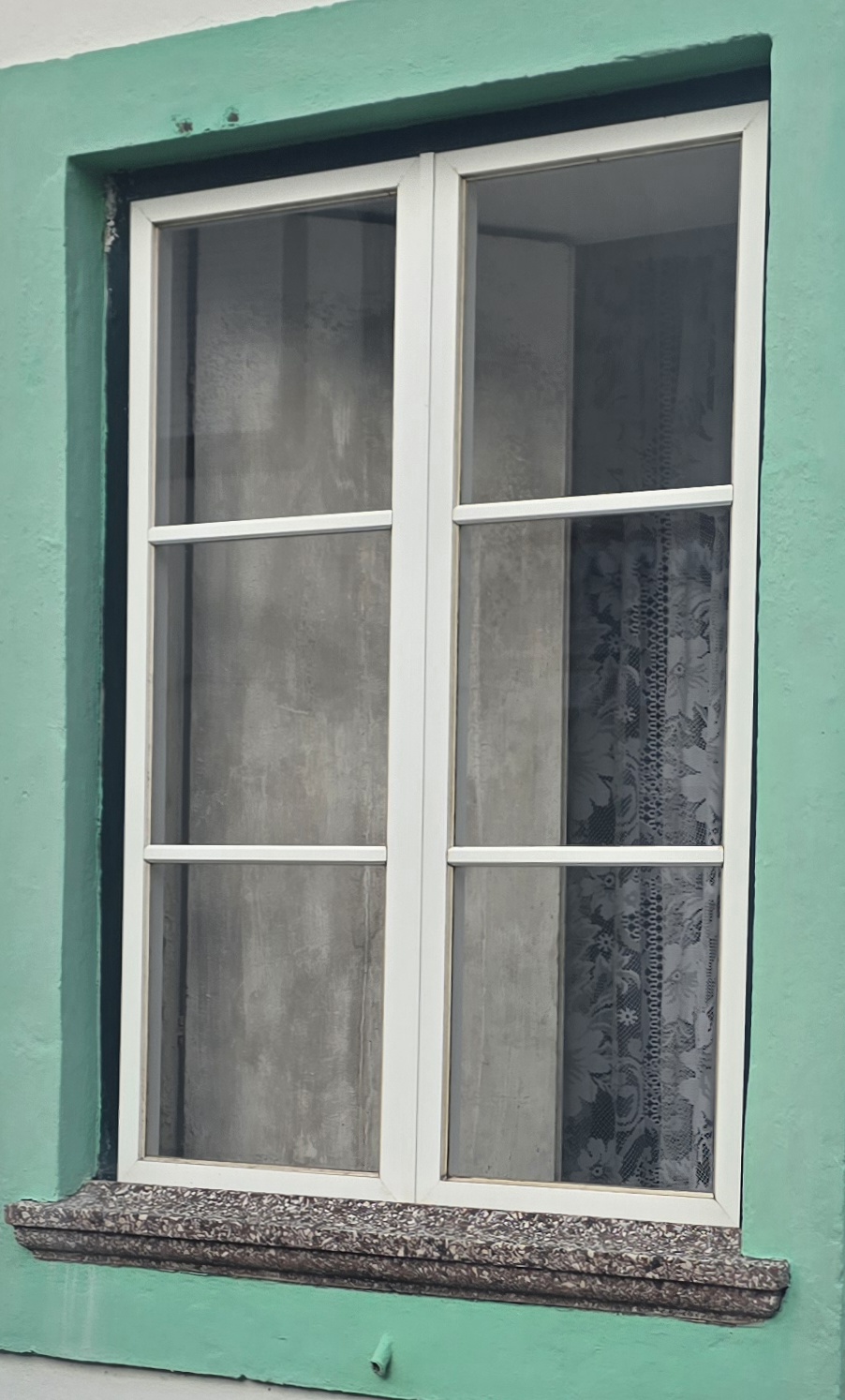 A white-framed six-pane window set in a mint-green painted wall, lace curtain behind the glass.