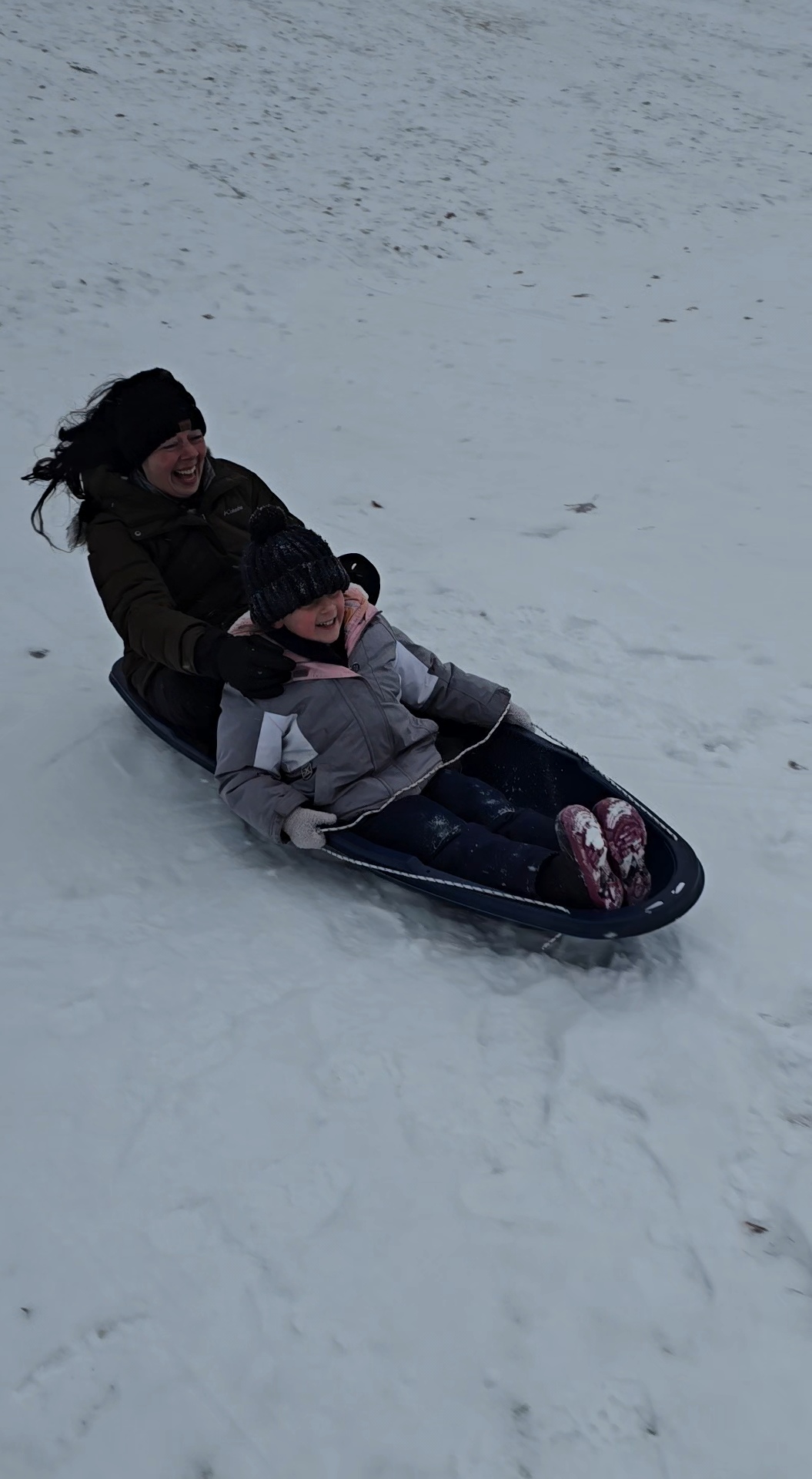 Nikki Bodie laughing as she and a little girl fly down a snowy Wisconsin hill on a sled.