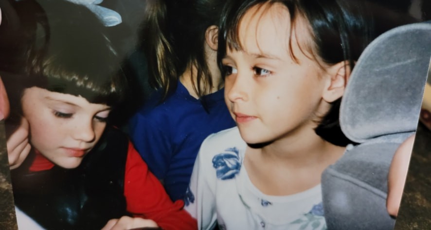 Nikki and Ali as young girls sitting close together at a party.
