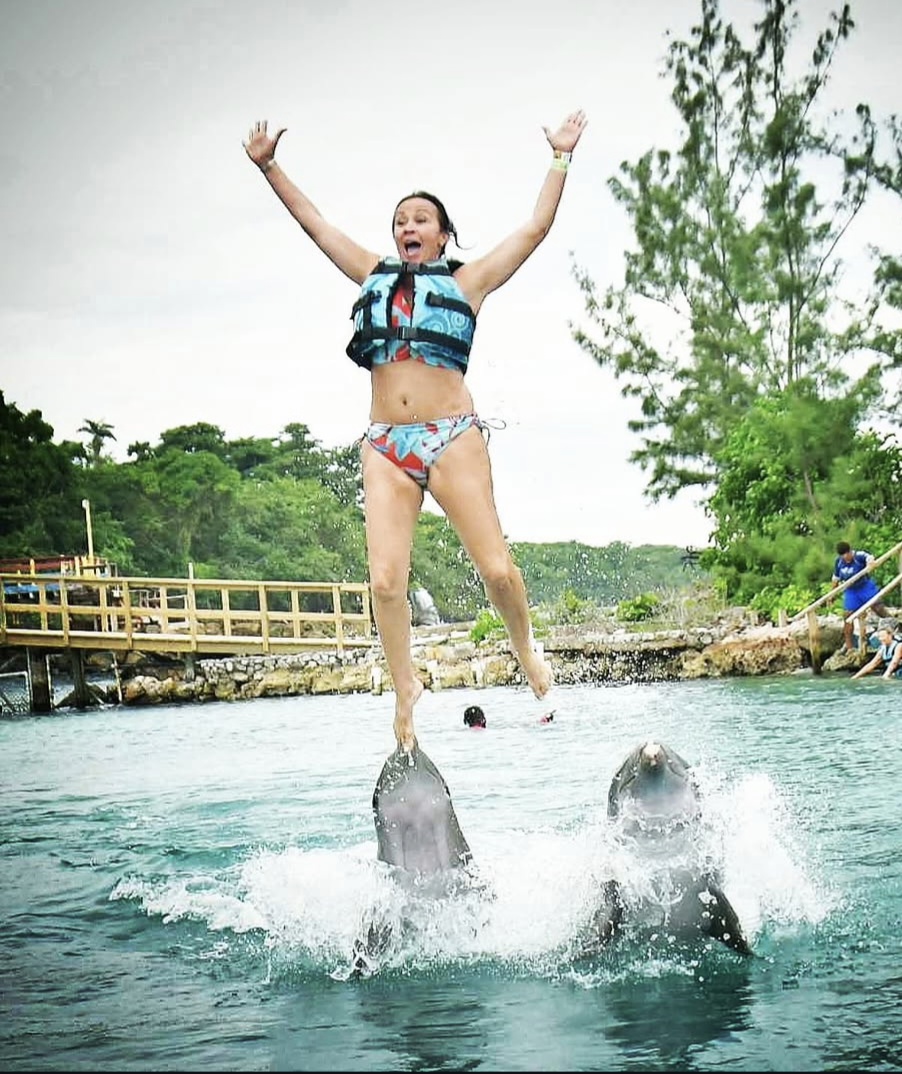 Patti launched into the air off the noses of two dolphins, arms up, mouth open in surprise.