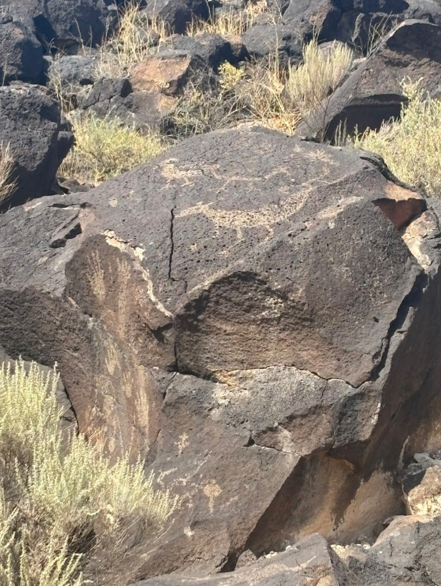 A close view of a carved figure and symbols on a reddish-brown boulder.