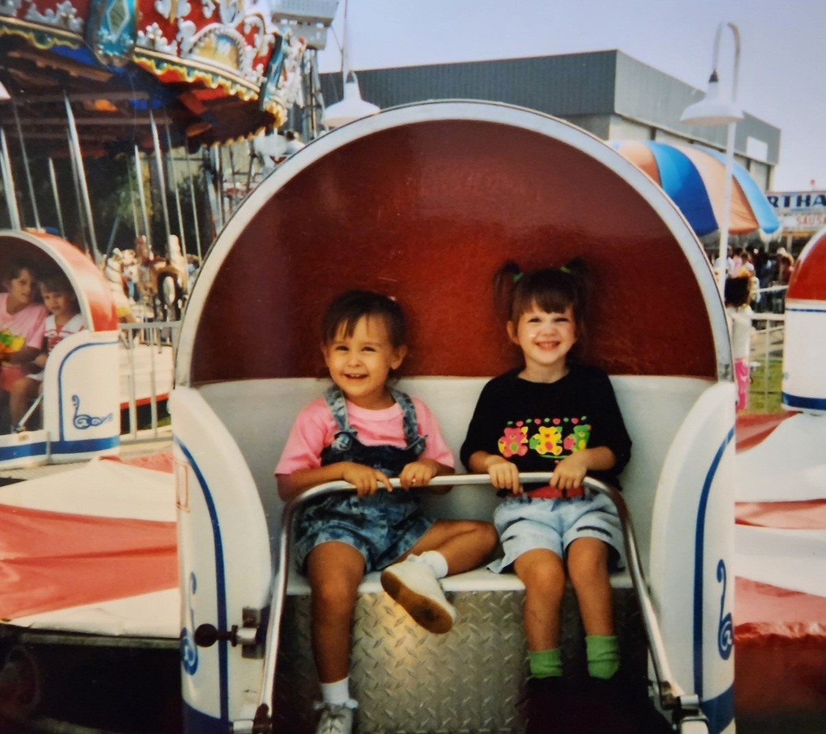 Nikki and Ali as small children riding together in a carnival teacup.