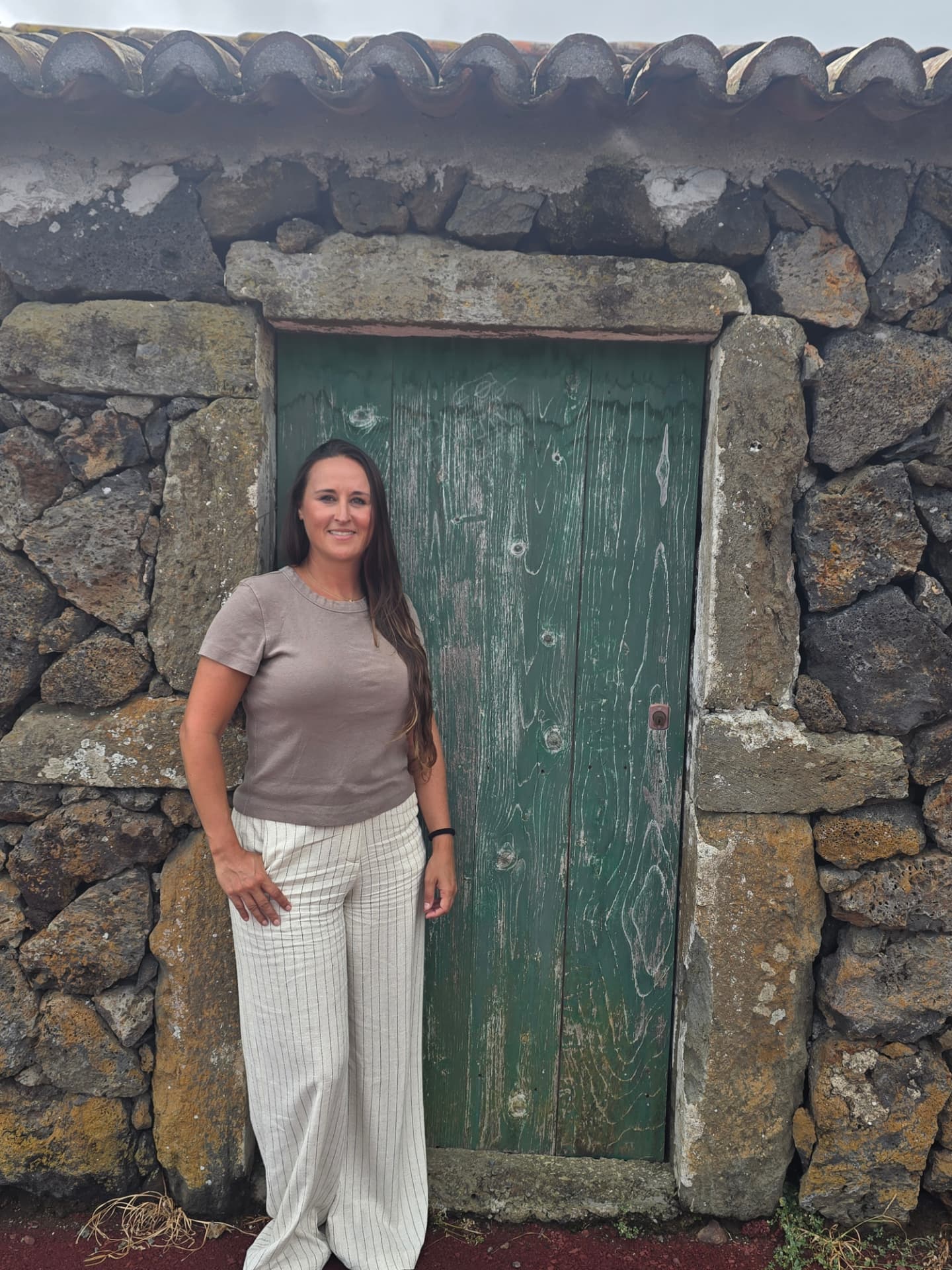 Nikki beside a weathered green door in a lava-stone wall.