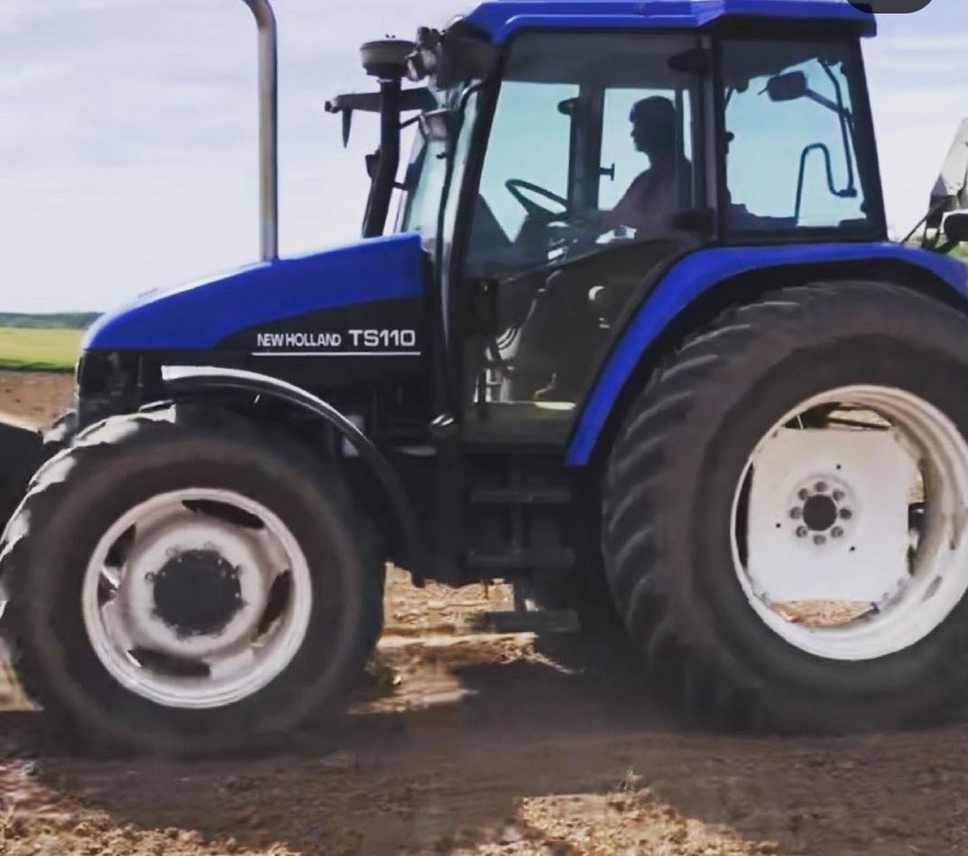 Nikki Bodie driving a blue New Holland tractor across a worked field.