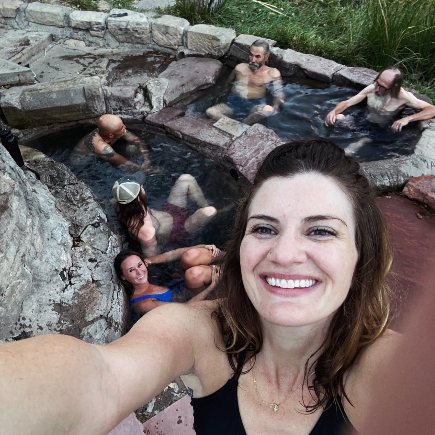 A selfie in a stone hot spring, other bathers soaking behind.