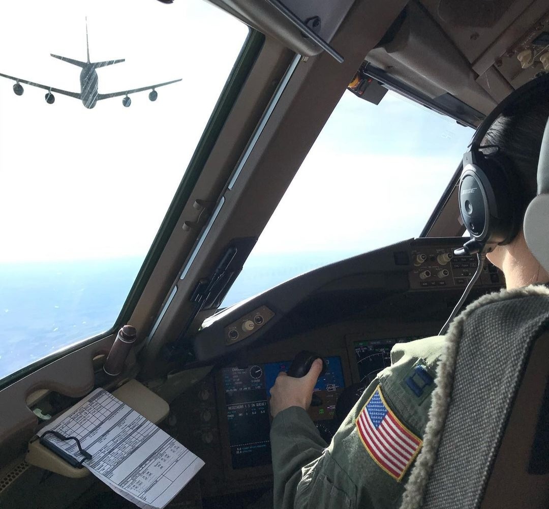 A pilot's hand on the controls as a KC-135 flies ahead through the windscreen.