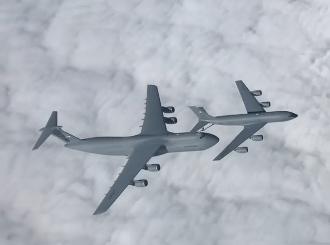 A C-5 and a KC-135 flying together above a sheet of clouds.