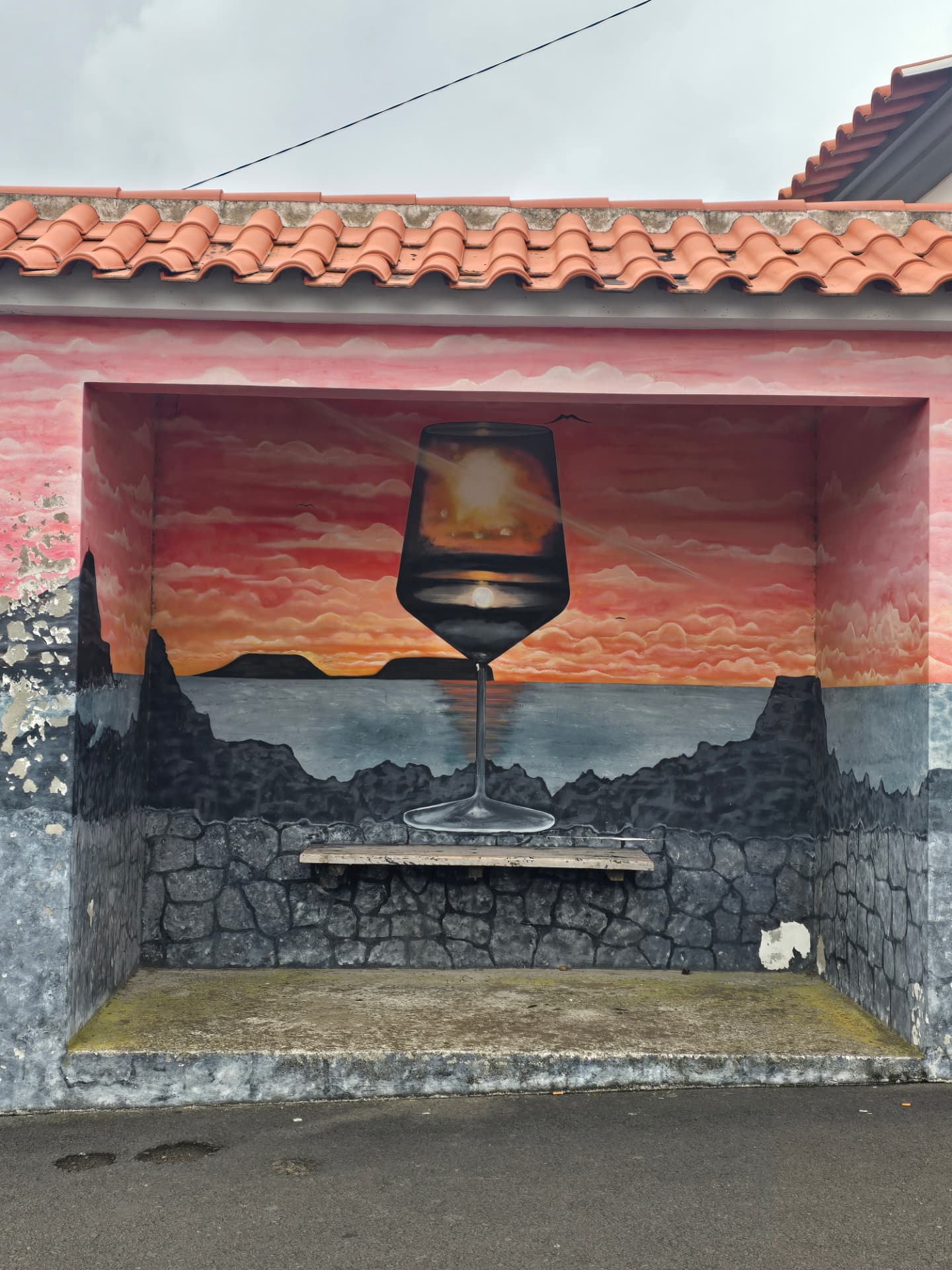 A bus-stop mural of a wine glass holding the sunset over volcanic rocks.