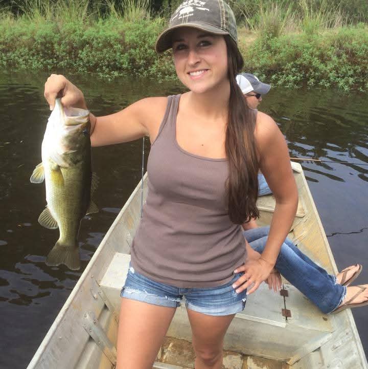 Nikki standing in a johnboat holding up a largemouth bass.