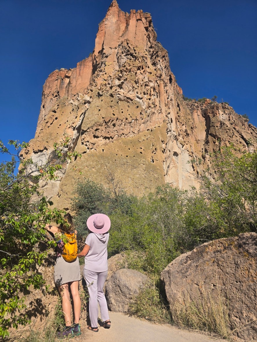 Nikki and Ali standing with their backs turned, looking up at a towering red rock spire at Bandelier.