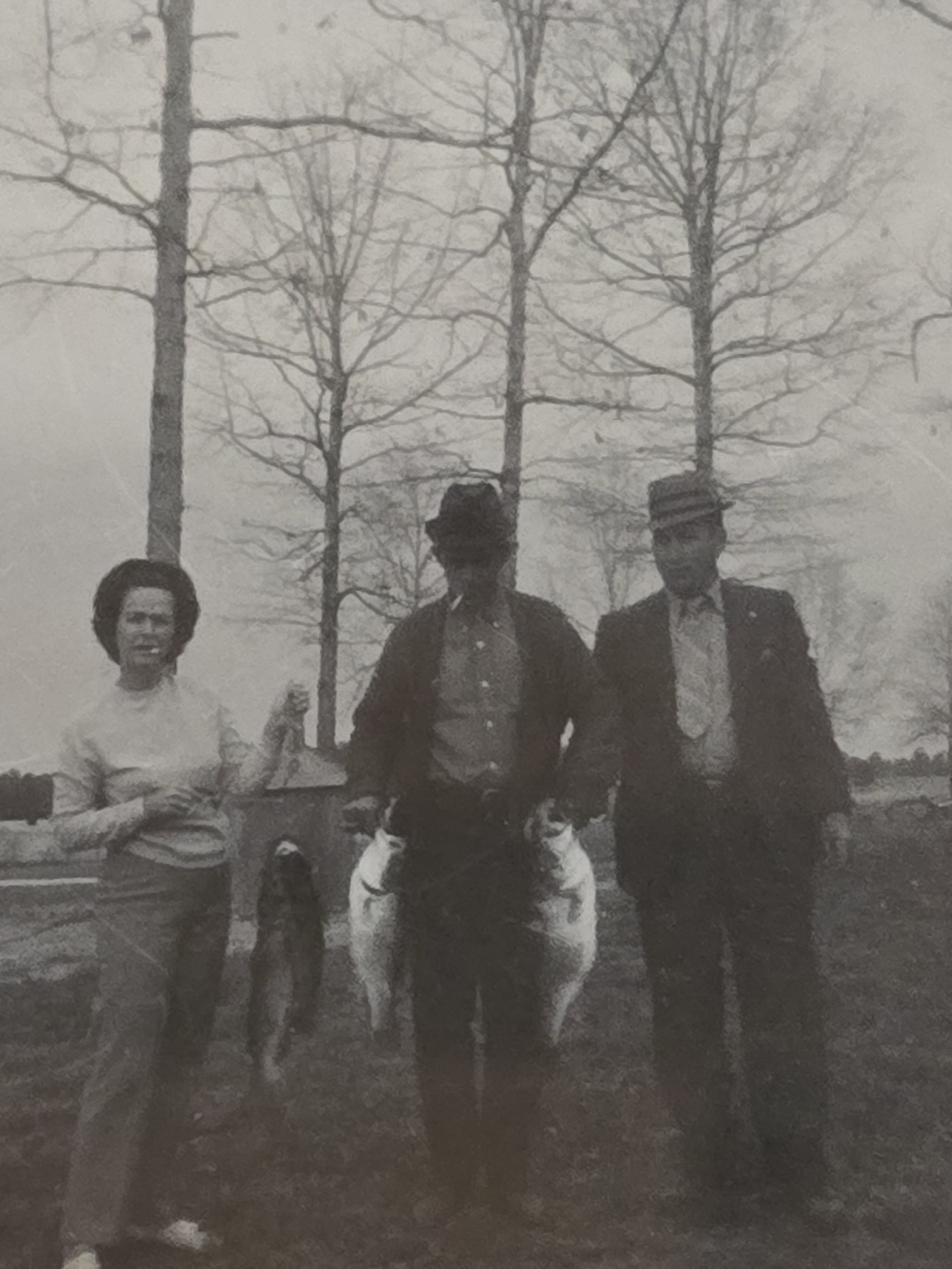 A black-and-white photograph of Grandma Reba, Granddaddy Fred holding a string of fish, and Reba’s brother beneath bare trees.