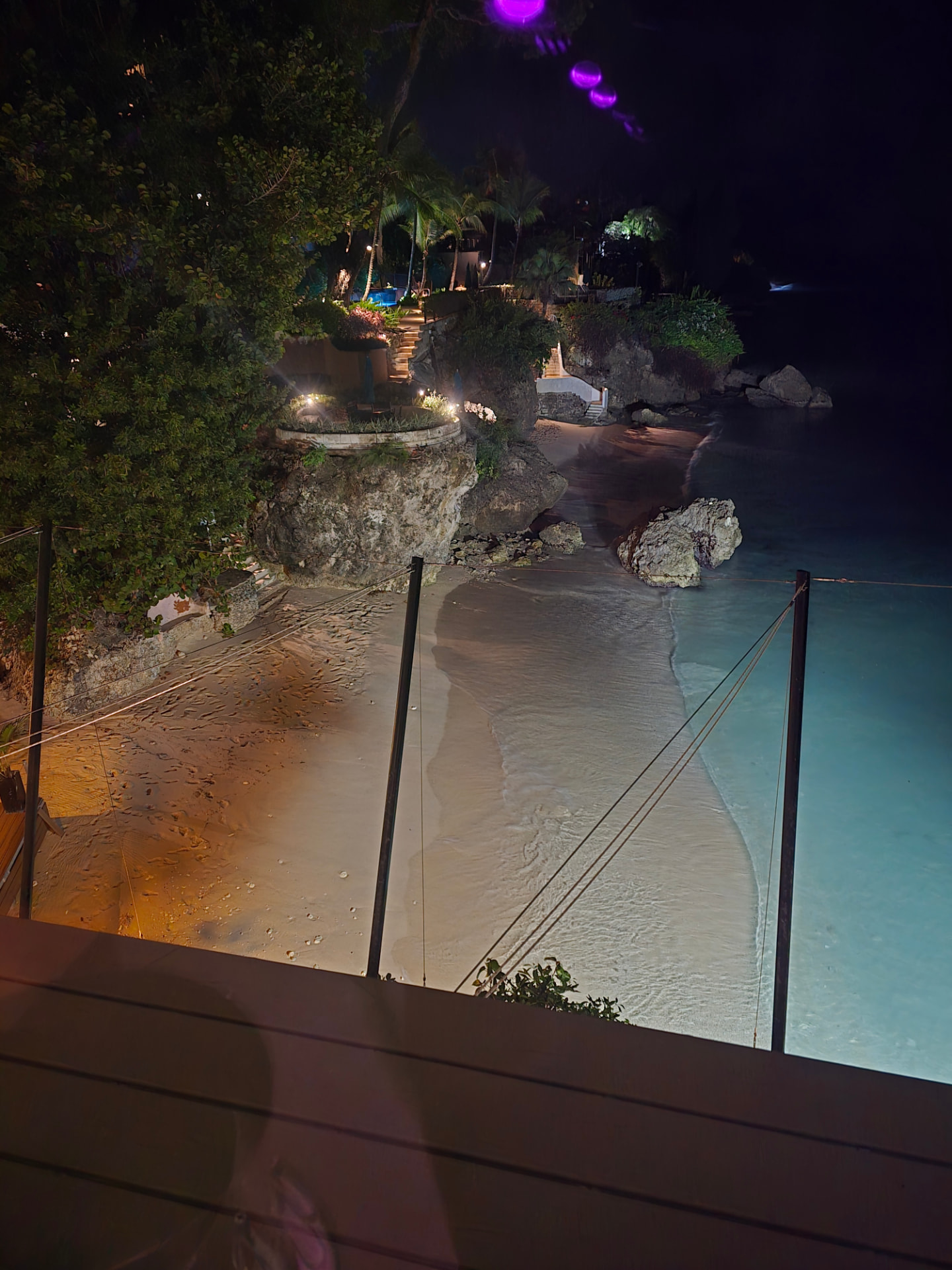 Night view down from The Cliff restaurant in Barbados to a lit cove of sand and glowing turquoise water.