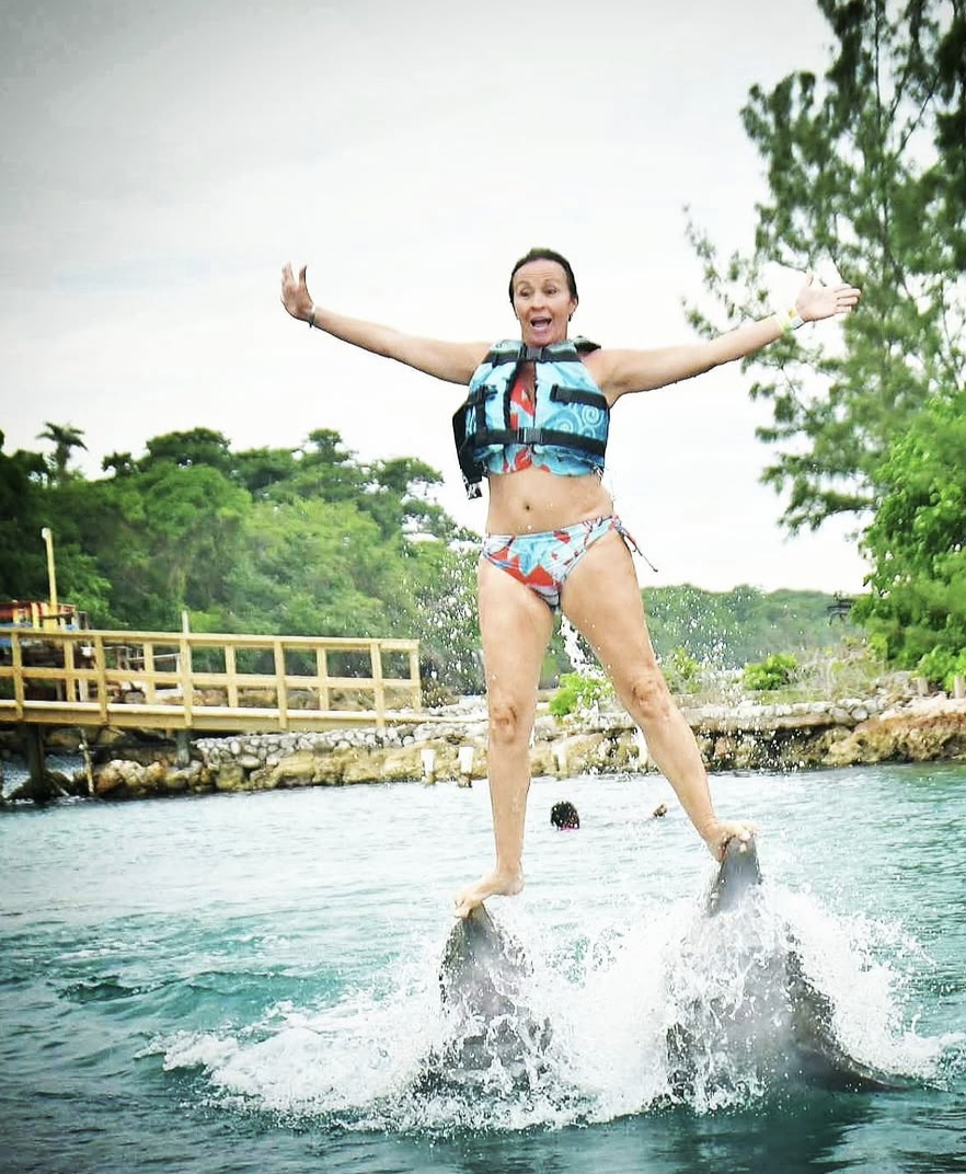 Patti standing on the noses of two dolphins, arms out.