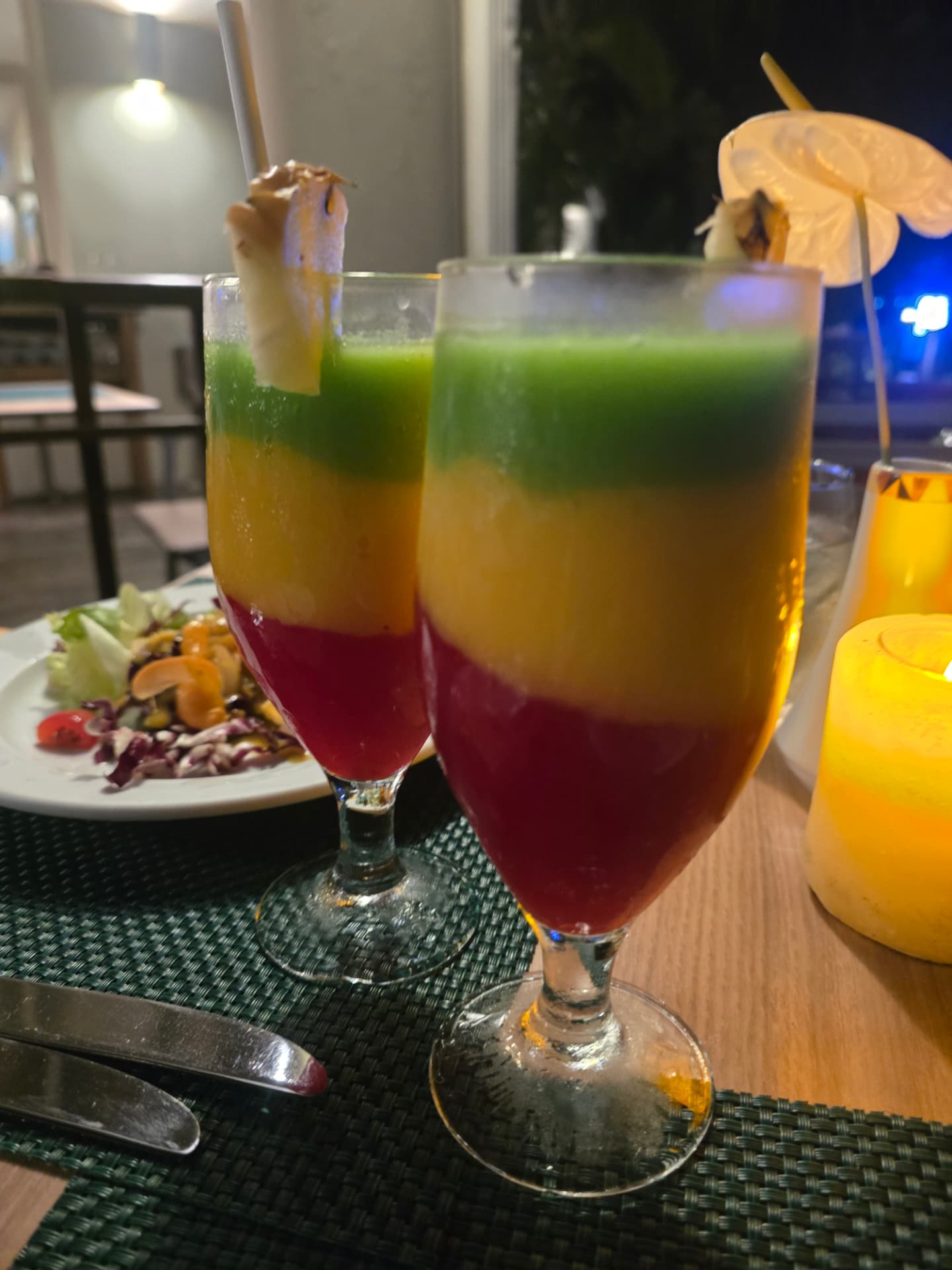 Two layered red, gold, and green drinks on a candlelit dinner table.