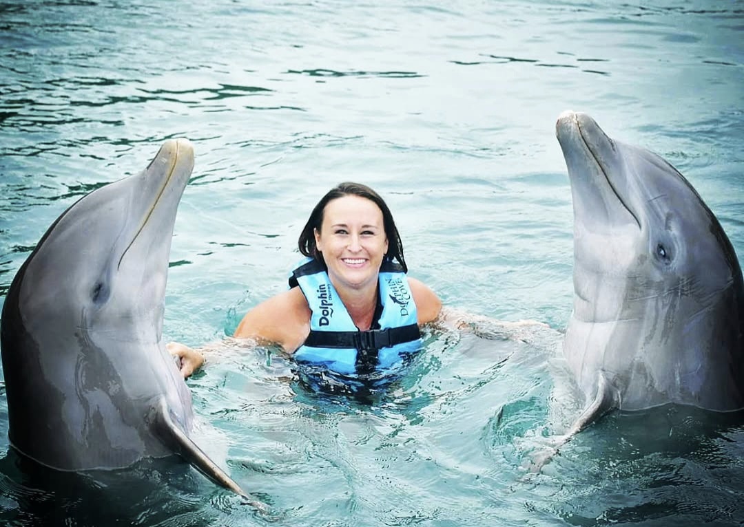Nikki in the water between two dolphins standing upright on either side of her.