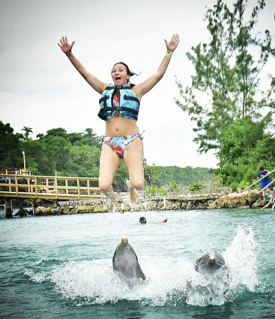 Patti high in the air above two dolphins, knees bent, arms raised.