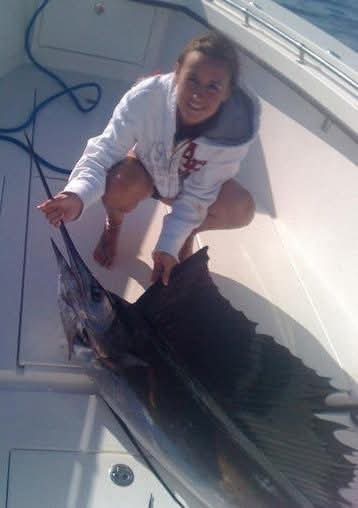 Nikki crouched on a boat deck beside a sailfish.