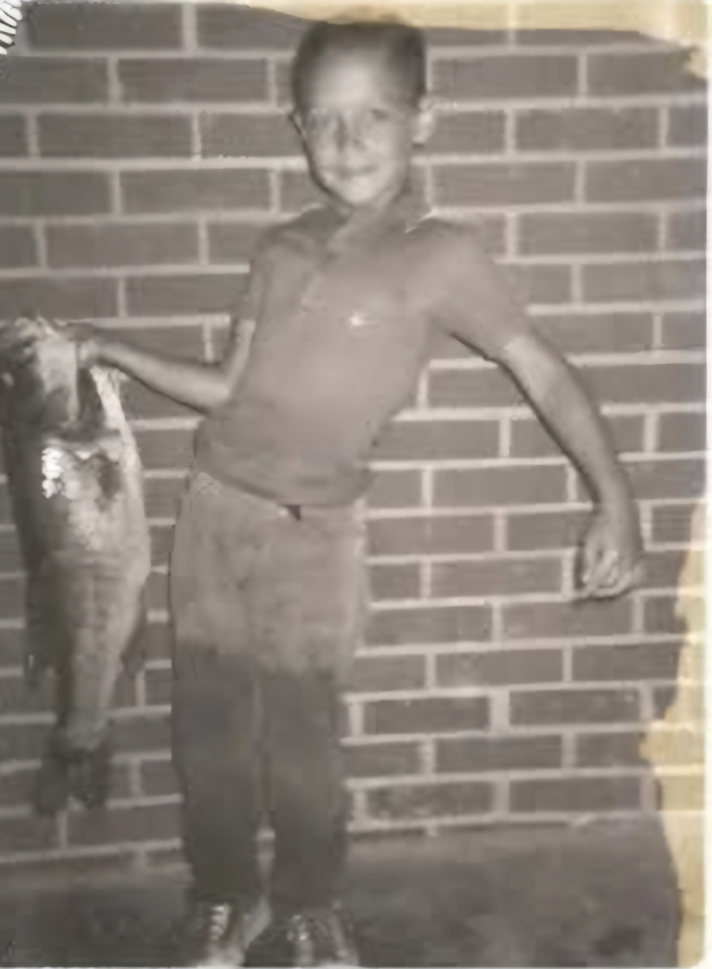 An old photograph of Nikki's dad as a boy, holding a big fish against a brick wall.