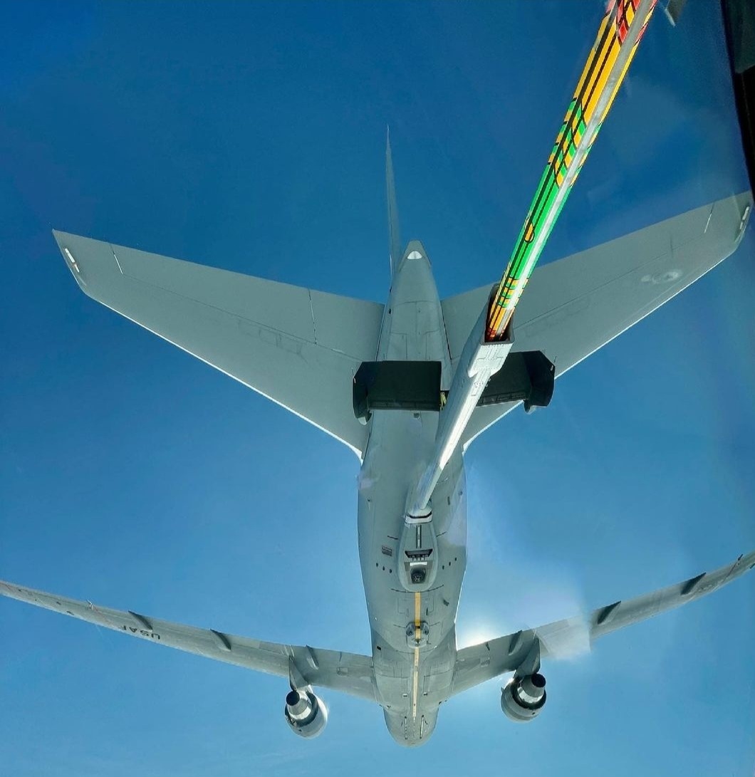 The painted refueling boom reaching toward a KC-46 in clear blue sky.