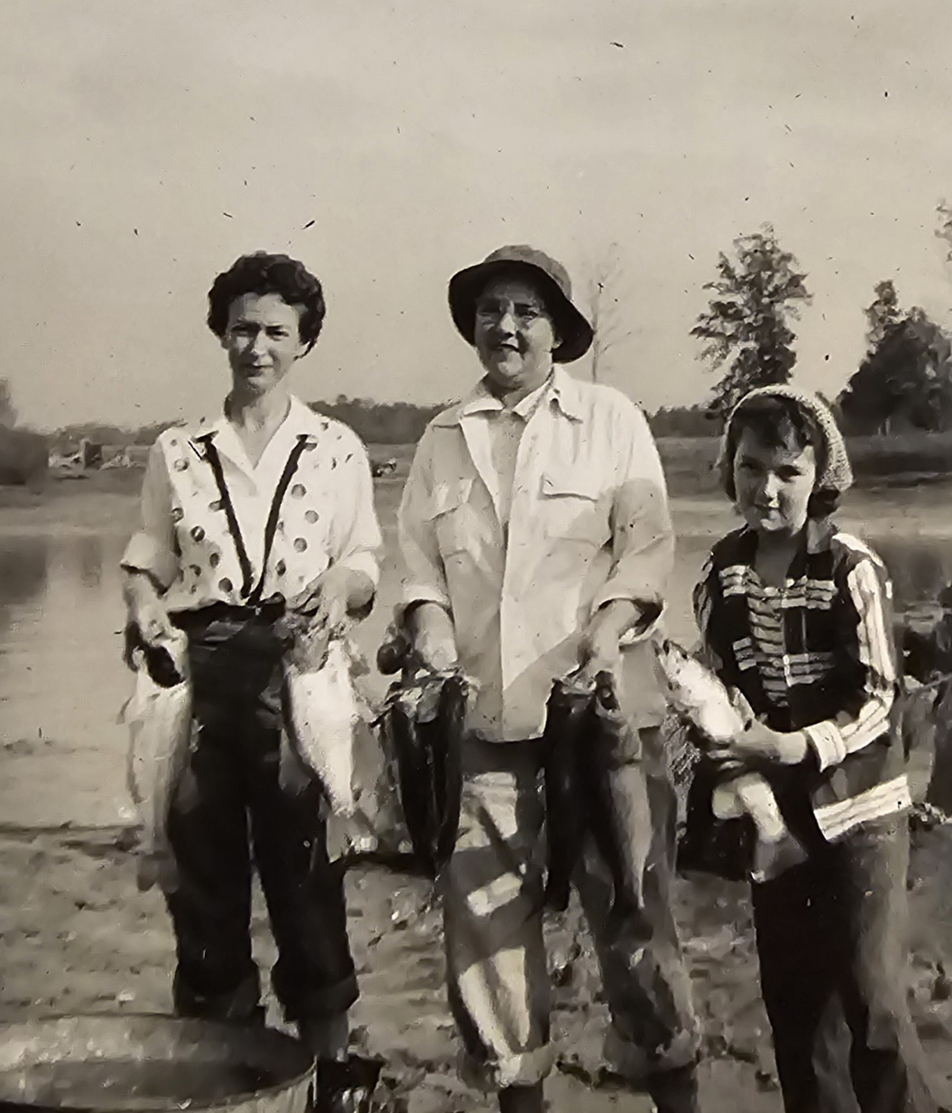 A black-and-white photograph of family holding strings of fish beside a pond, Grandma Reba among them.