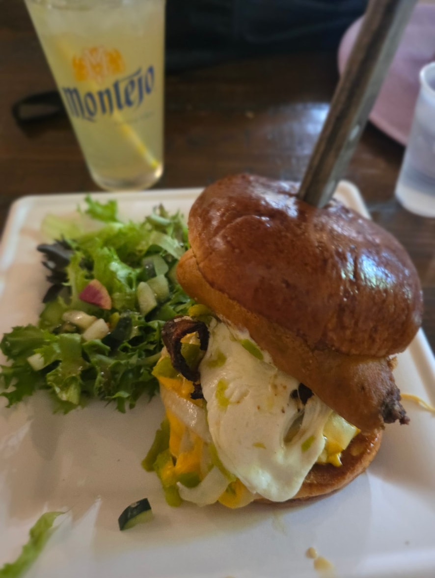 A burger with a fried egg beside a green salad and a Montejo beer.