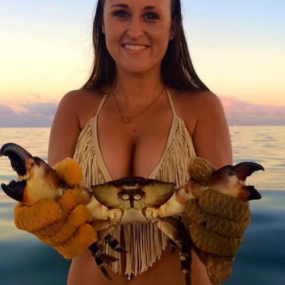 Nikki at sunset on the water holding a stone crab in gloved hands.