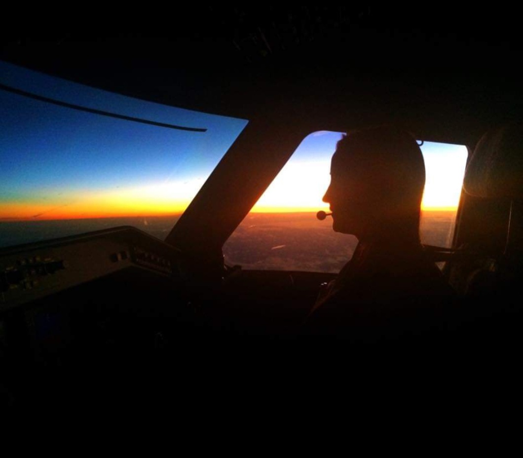 Nikki Bodie silhouetted at the controls of a flight deck at altitude, a burning sunset horizon through the windscreen.