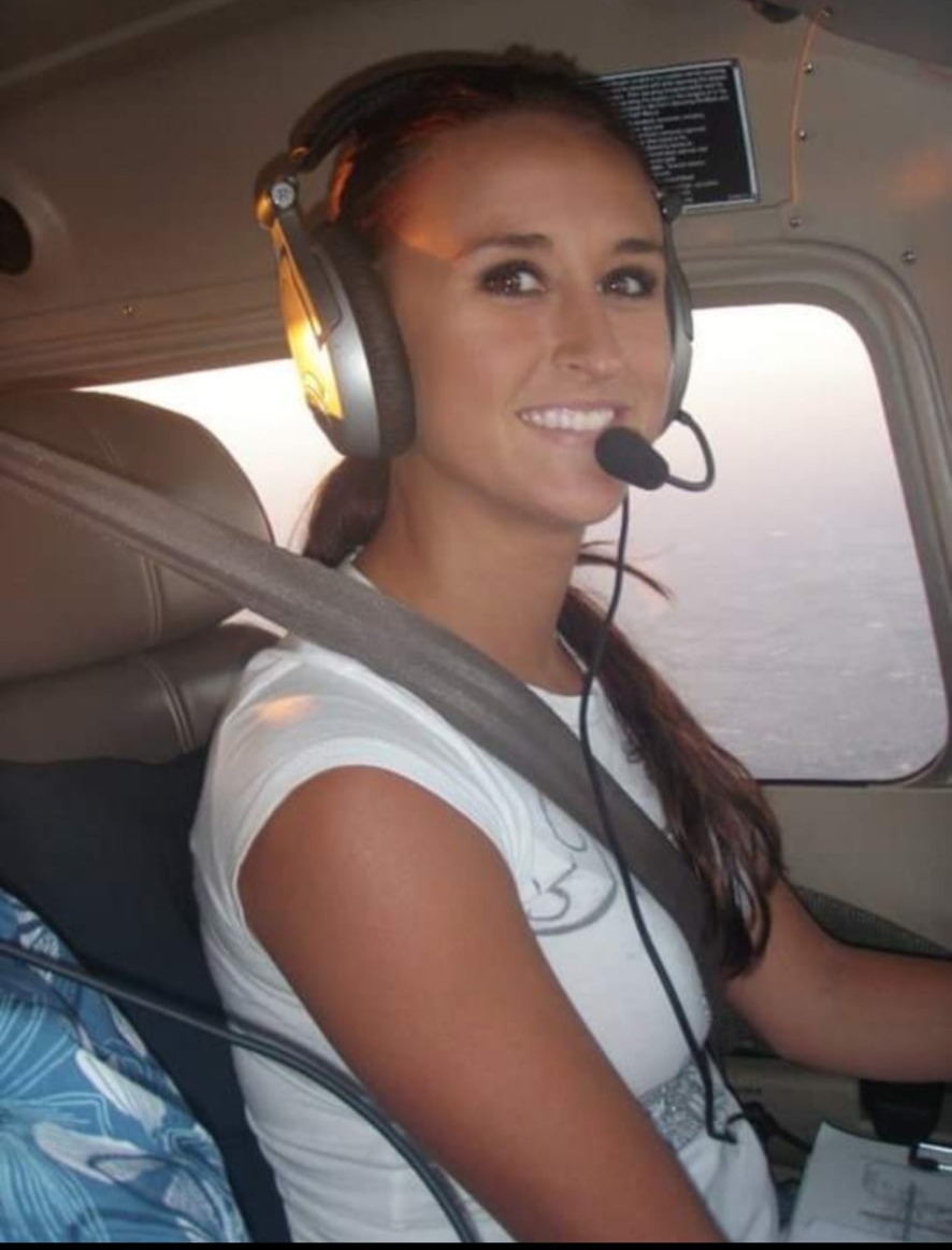 Young Nikki smiling in a headset at the controls of a small training airplane.
