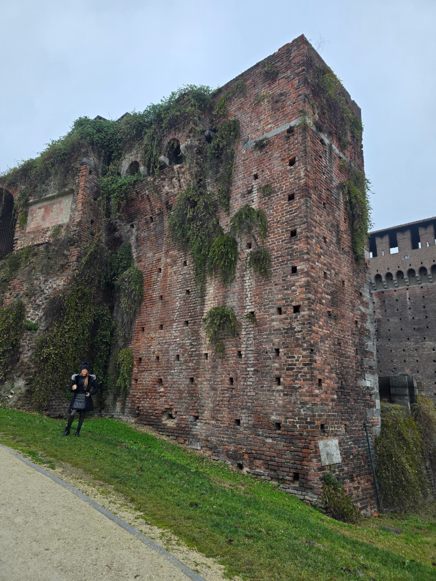 An ivy-covered brick tower of an old castle wall under a grey sky.