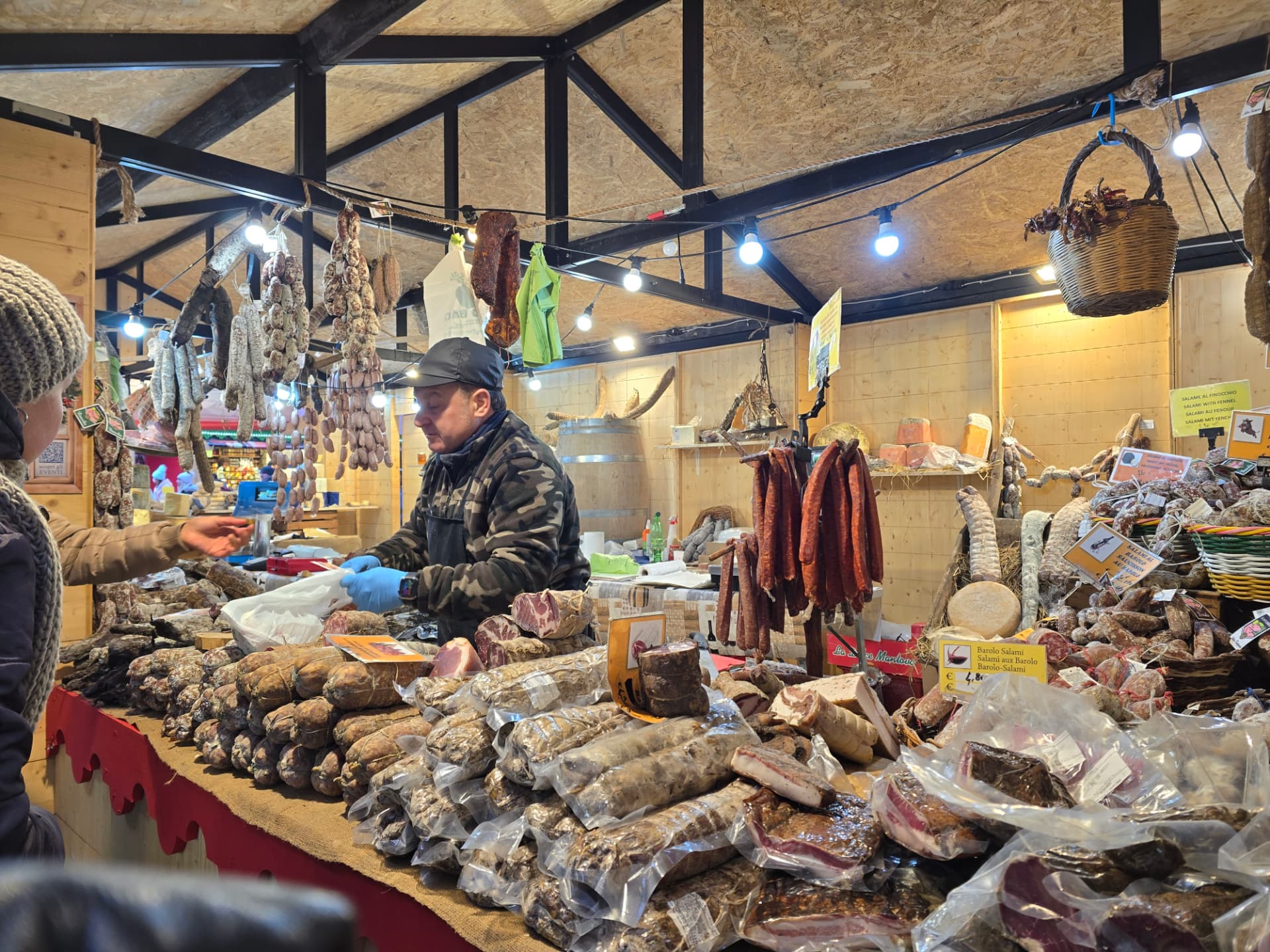 A market vendor behind a counter piled with Italian salami and cured meats.