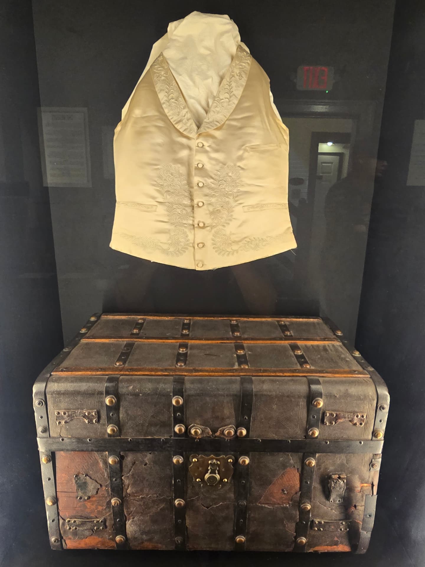 Poe's travelling trunk, wood bound in leather and iron straps, displayed beneath a cream embroidered silk waistcoat.