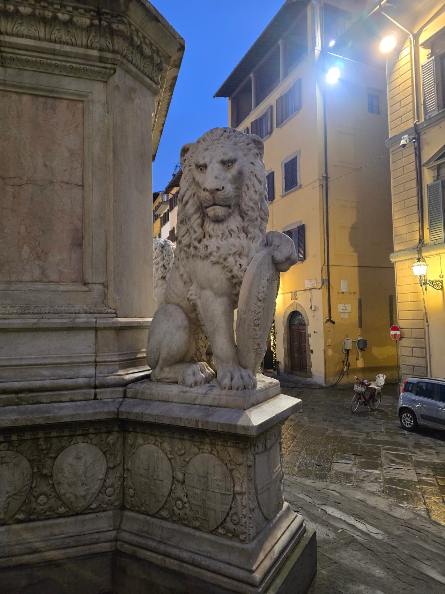 A stone lion statue on a pedestal on a rainy Florence street at night.