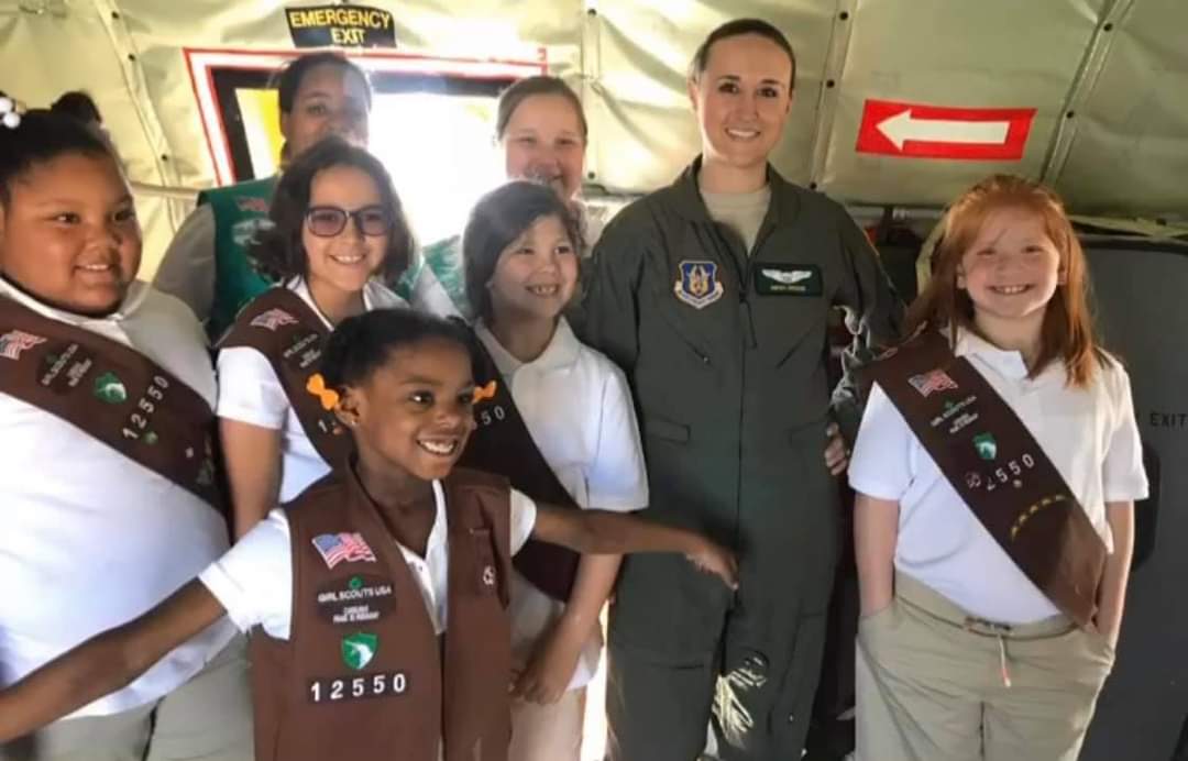 Nikki in her flight suit with a troop of Girl Scouts inside a military plane.
