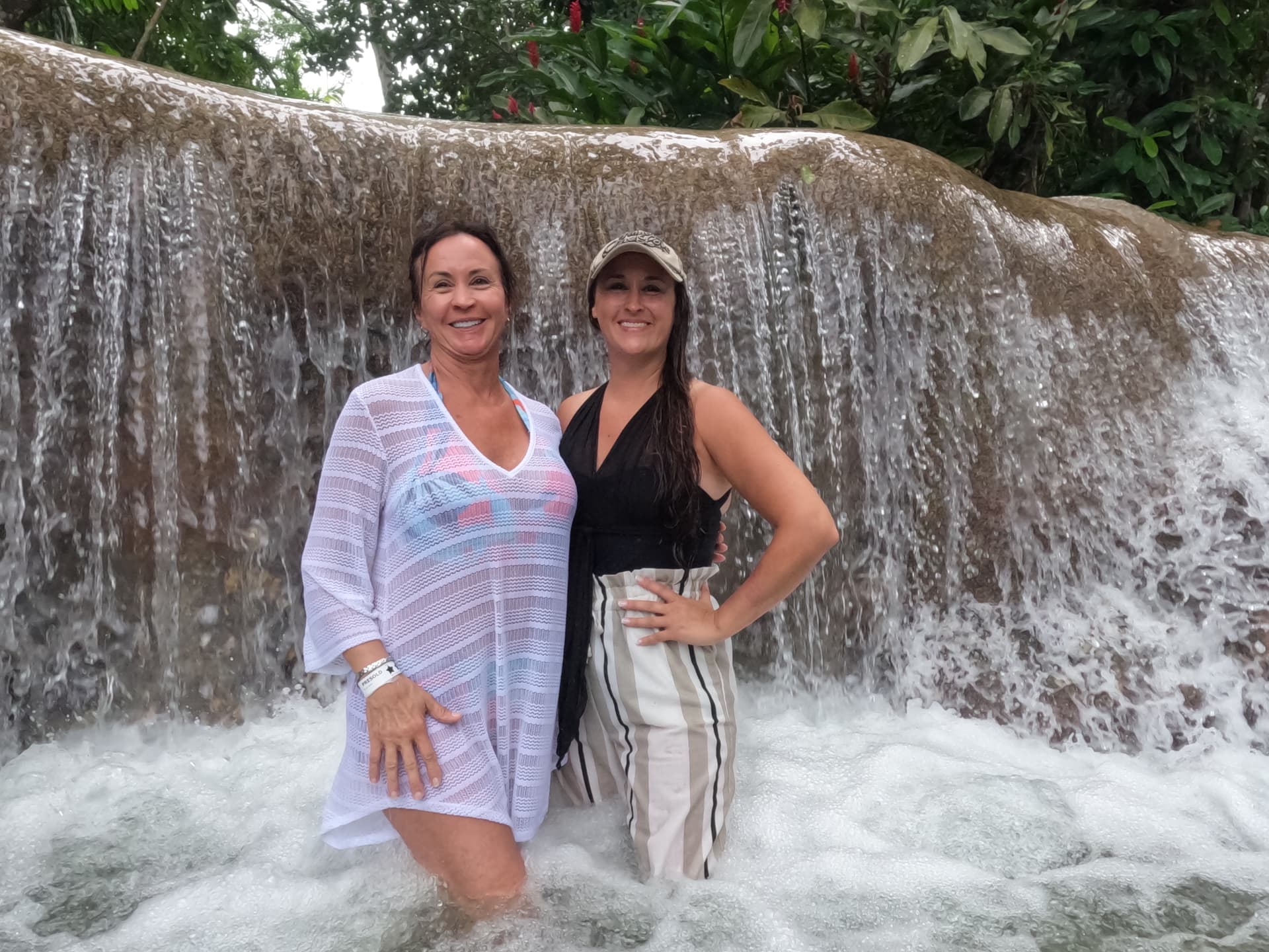 Patti and Nikki standing together in Dunn's River Falls, the waterfall pouring behind them.