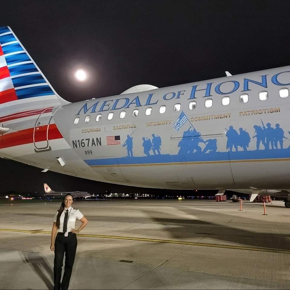 Nikki in uniform beside American's Medal of Honor airplane at night before a Valor Flight, full moon above.