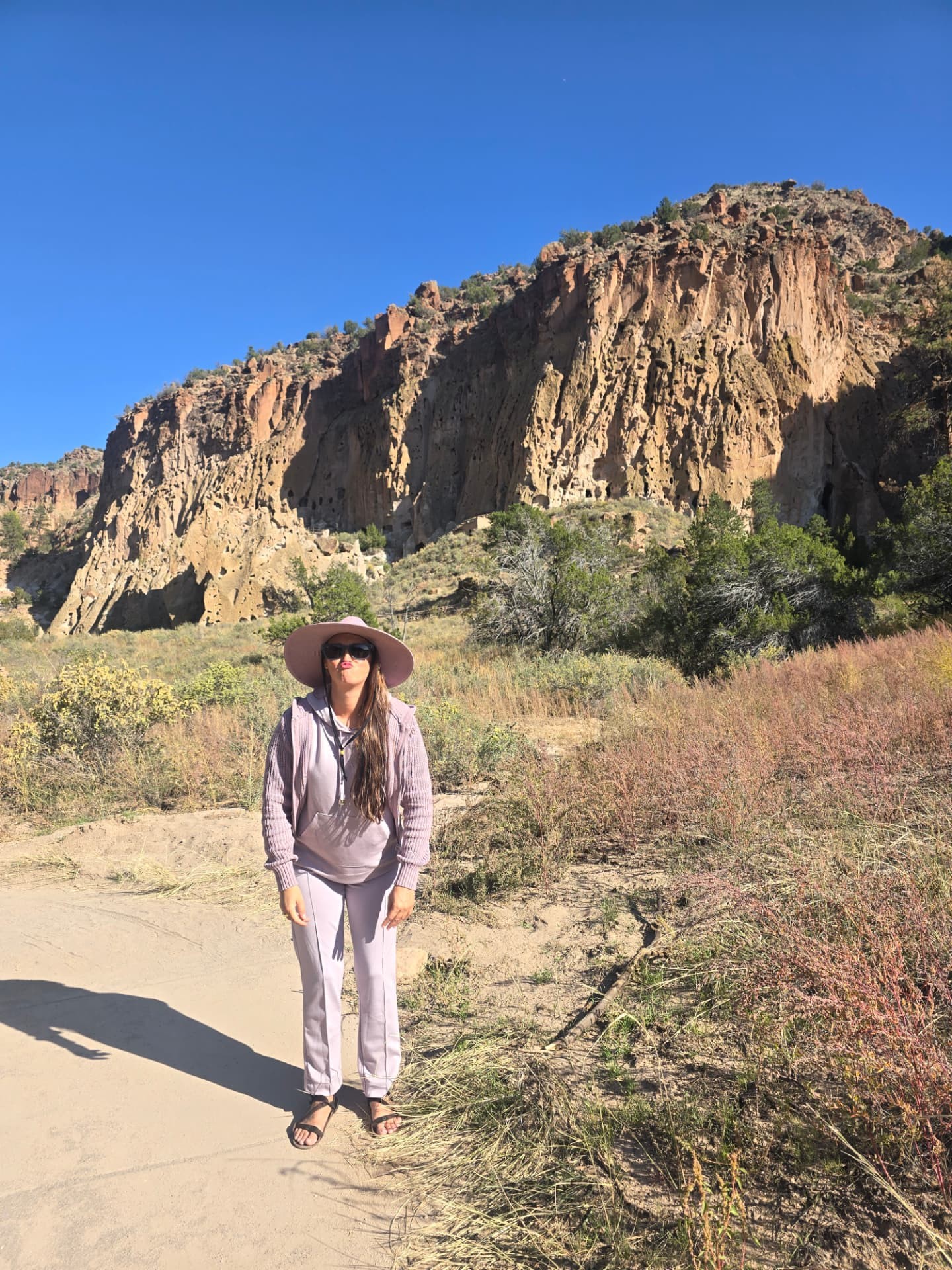 Nikki in a pink hat blowing a kiss below the cliffs of Frijoles Canyon.