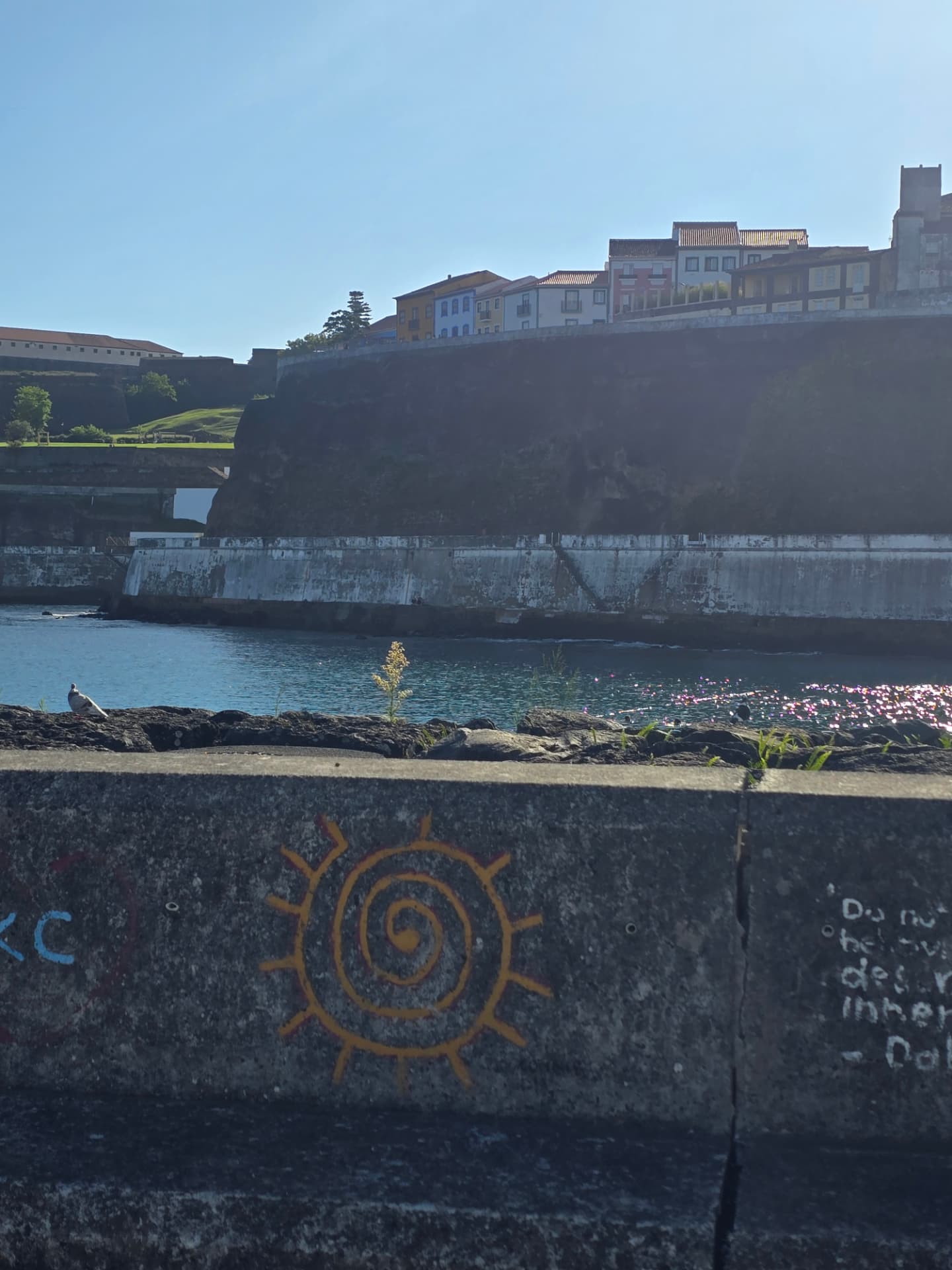 A painted sun spiral on a harbor wall beneath old Angra fortifications.