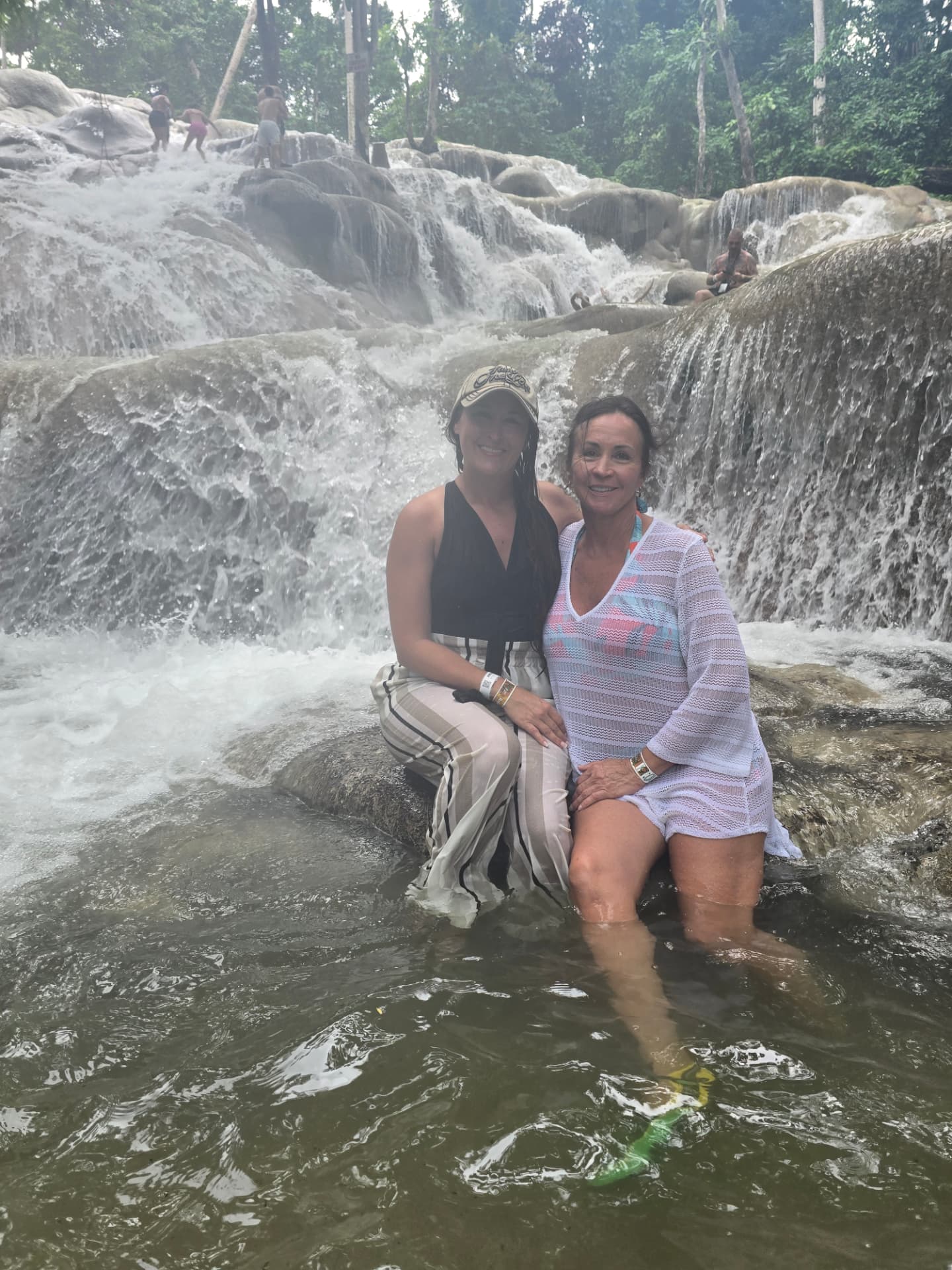 Nikki and Patti sitting on a rock in the cascading water of Dunn's River Falls.