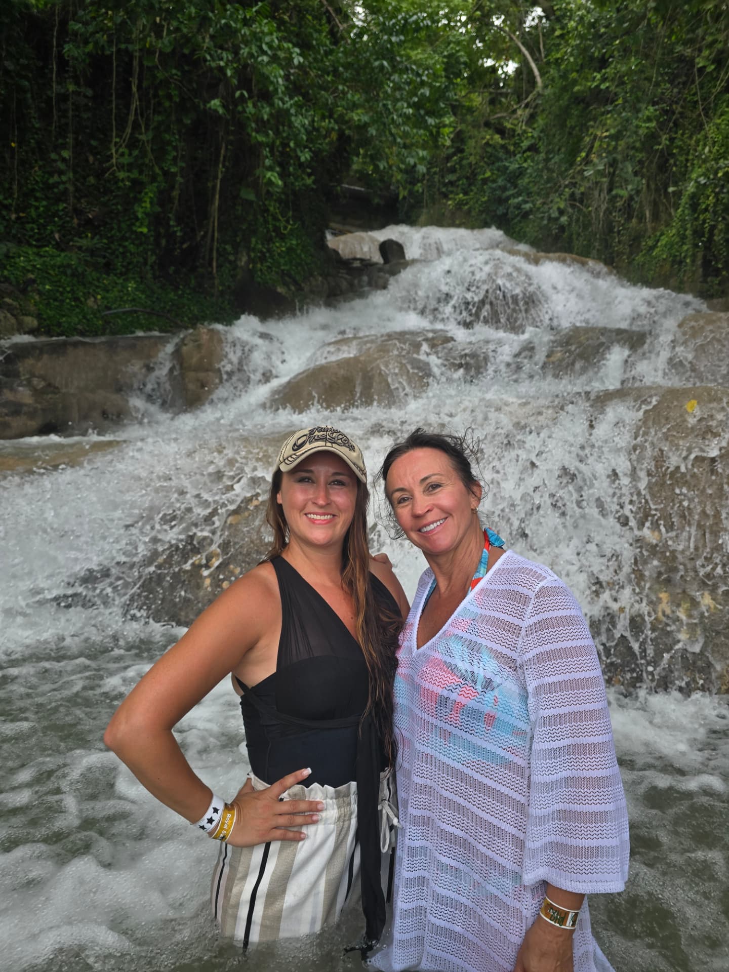 Nikki and Patti standing in the water at the foot of Dunn's River Falls, the cascade rising behind them.