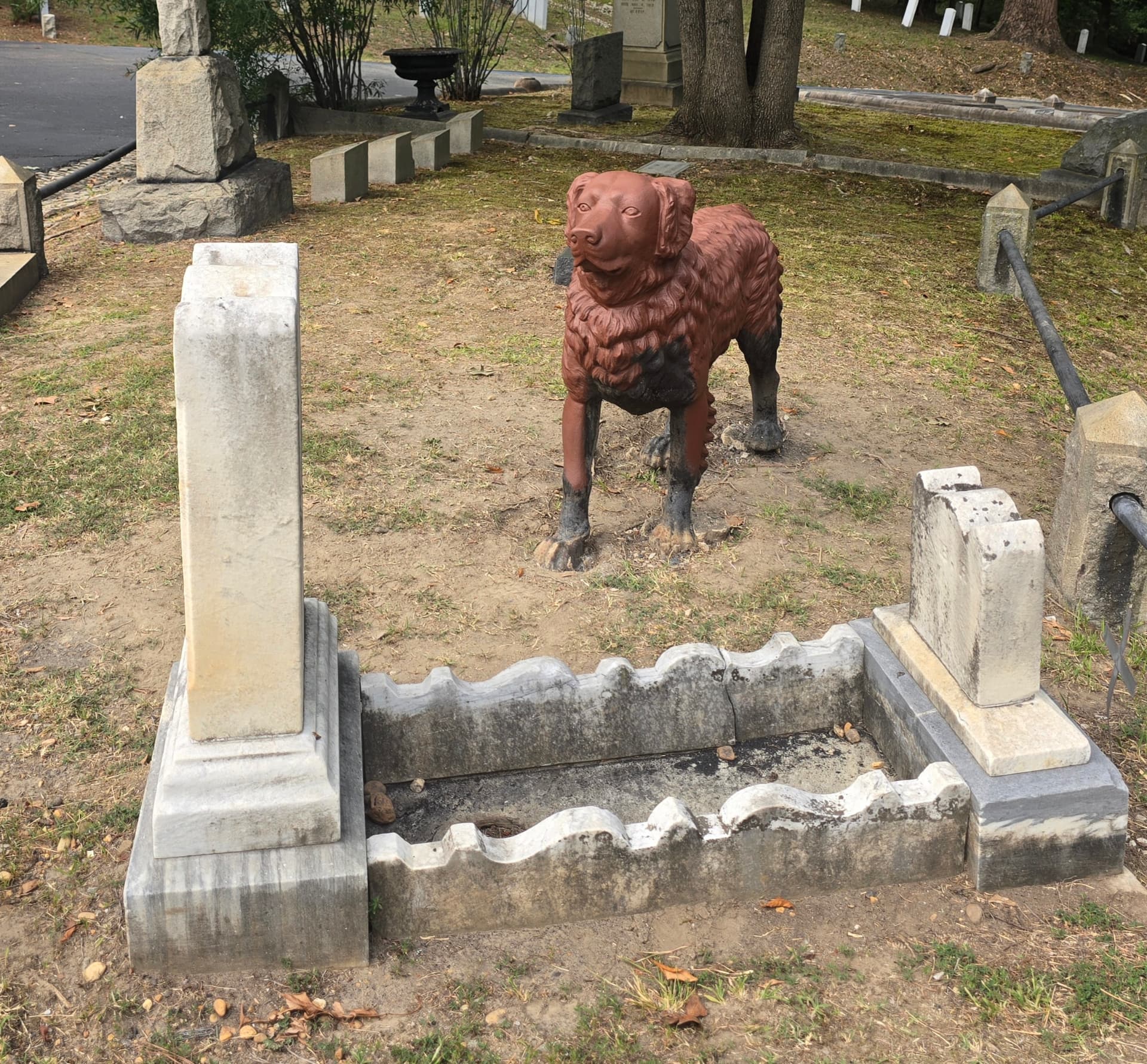 The cast-iron dog of Hollywood Cemetery standing watch over a low marble grave enclosure.