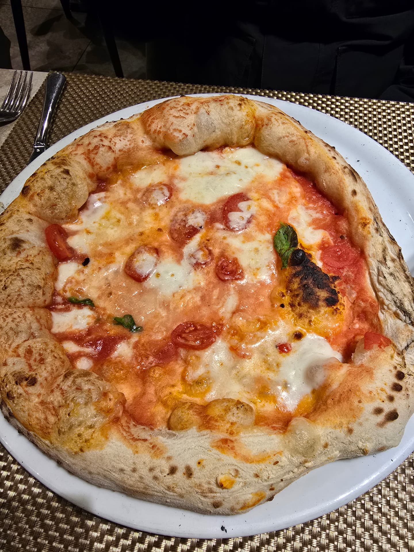 A blistered margherita pizza with cherry tomatoes, mozzarella, and basil.
