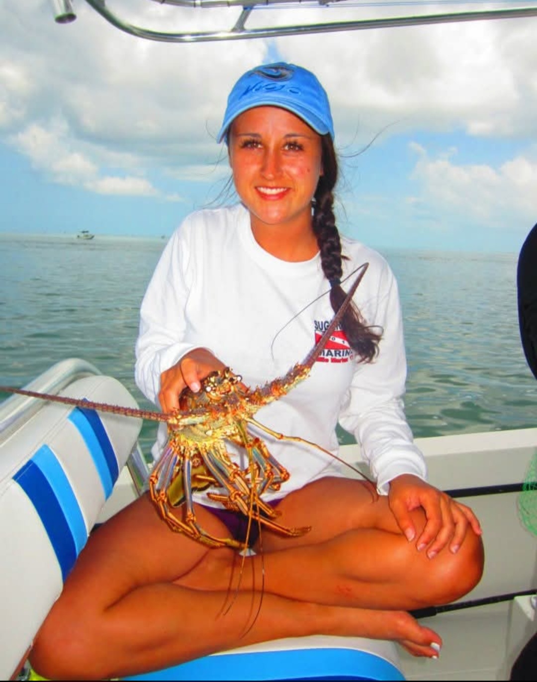 Nikki sitting cross-legged on a boat holding a spiny lobster.