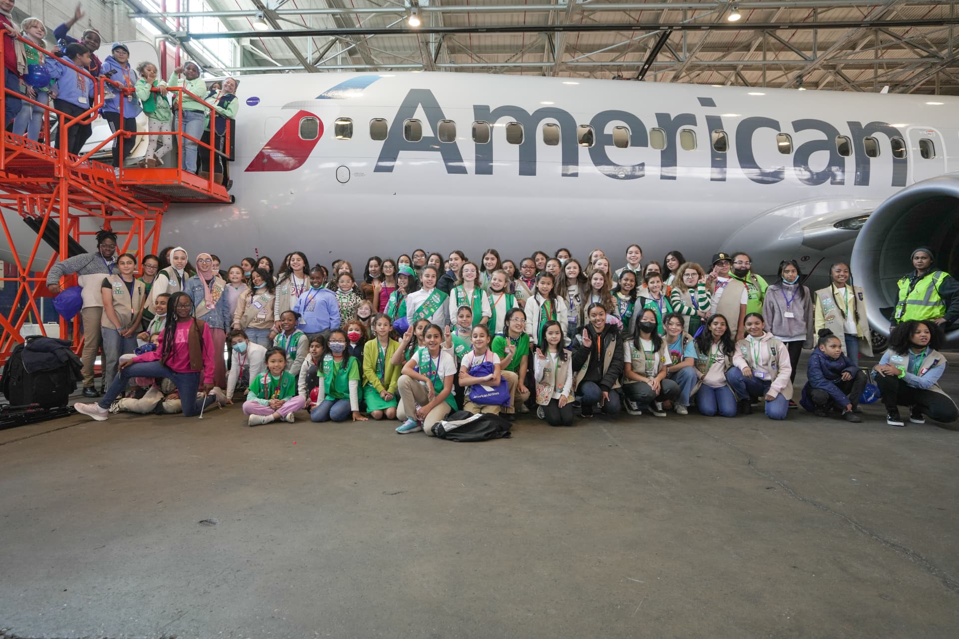A large group of Girl Scouts gathered in front of an American Airlines jet in the hangar.