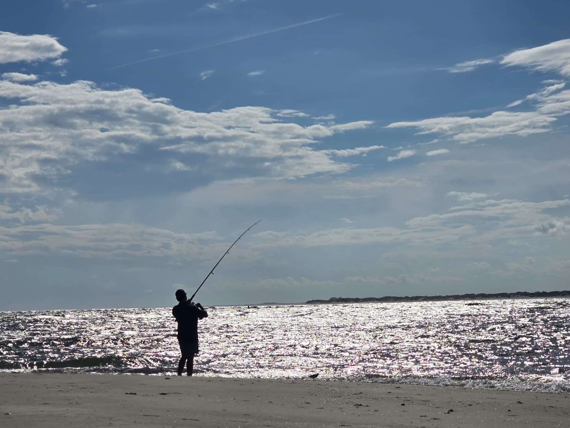 Slayter silhouetted against glittering water, casting from the beach at Emerald Isle.