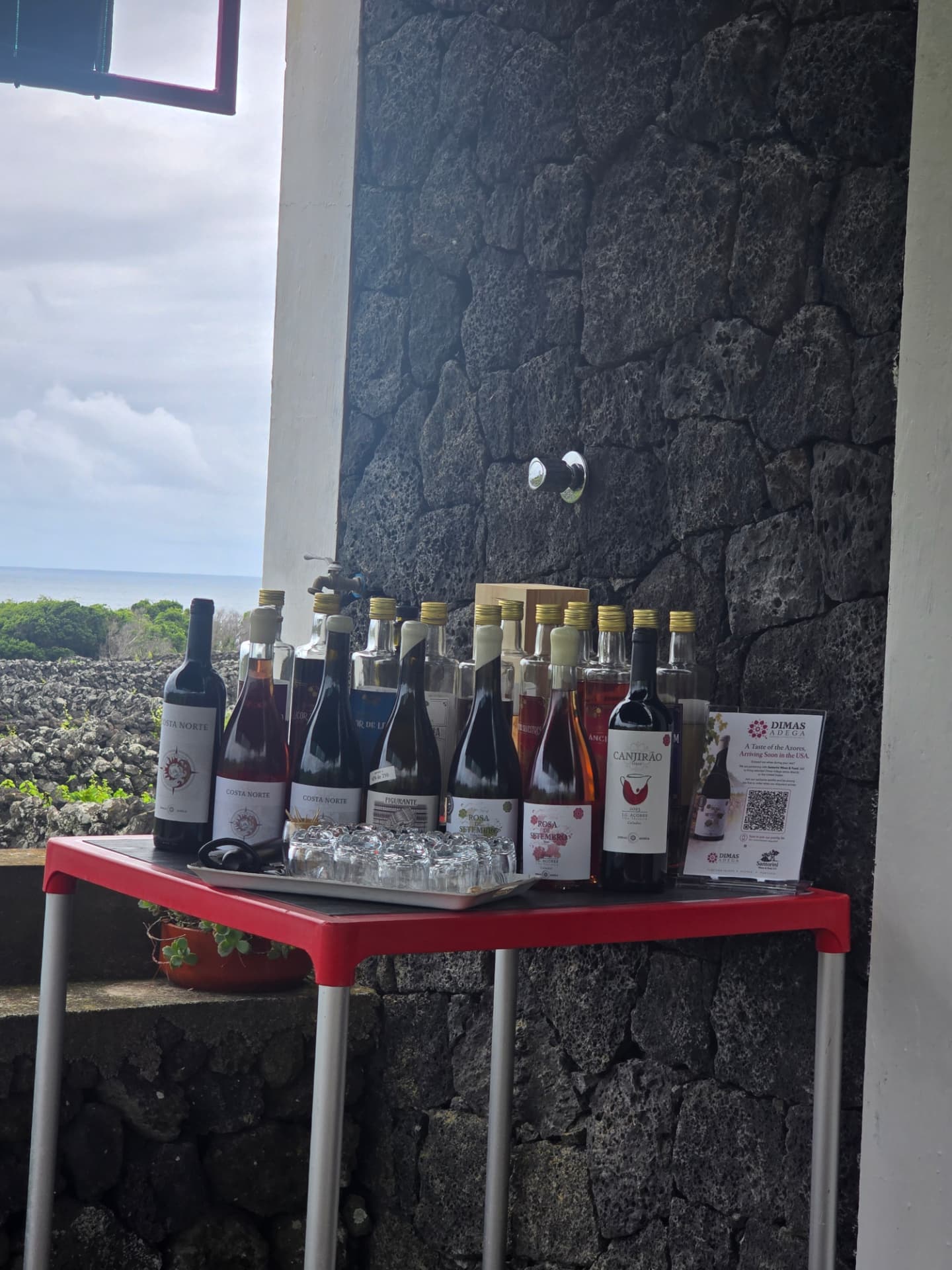 Wines on a red table against black volcanic stone at Dimas Adega, ocean beyond.