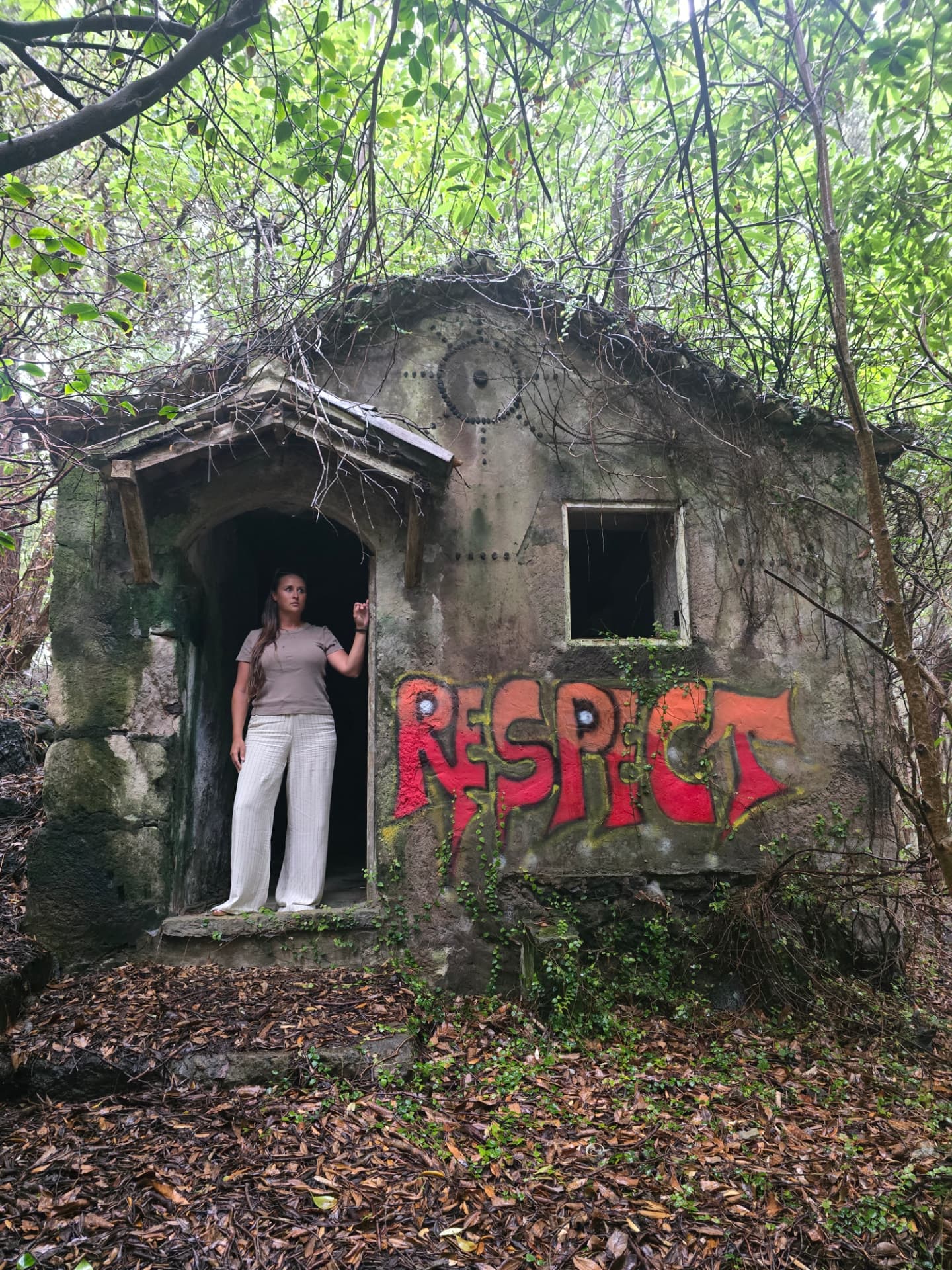 Nikki in the doorway of an abandoned building in the woods, RESPECT graffiti on the wall.