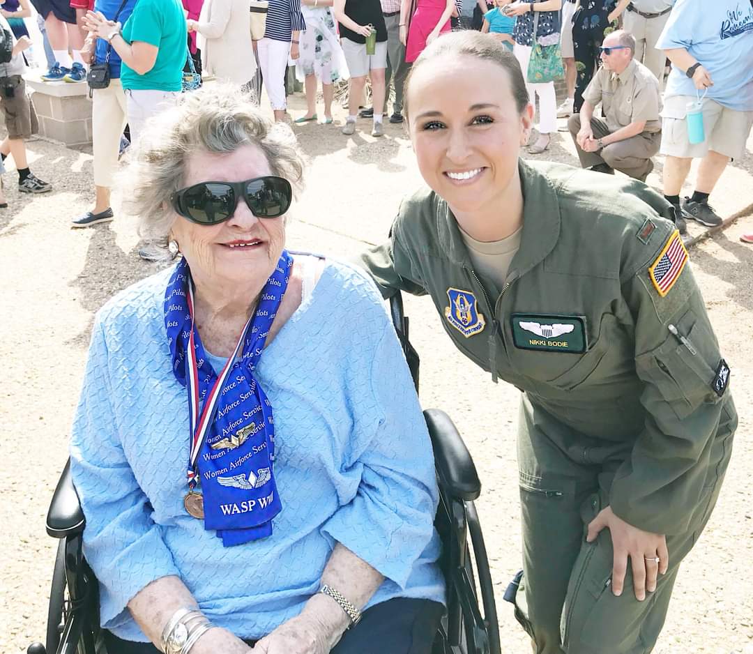 Nikki in her flight suit smiling beside a WASP wearing her medal and sunglasses.