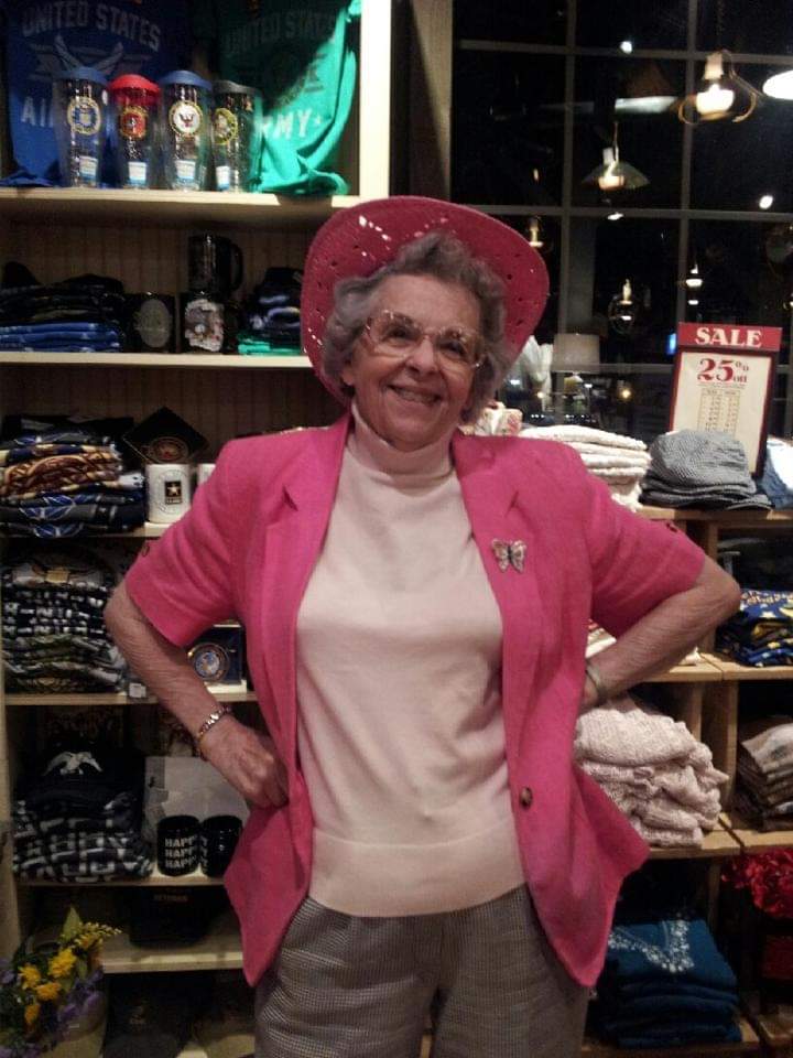 Granny Louese smiling in a pink jacket and hat, her butterfly brooch pinned to her lapel.