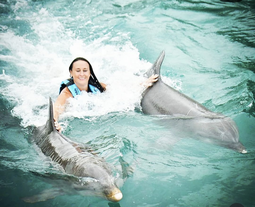 Nikki pulled through the water between two dolphins, holding their dorsal fins.